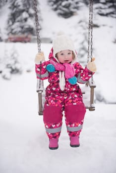 child outdoor in park at winter day with fresh snow, cute little girl swing and playing