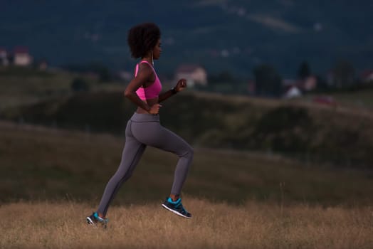young African american woman runner with headphones jogging outdoors in nature beautiful summer night - Fitness, people and healthy lifestyle