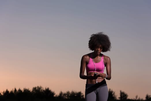 portrait of a young beautiful african american woman with headphones and mobile phone jogging in nature beautiful summer night