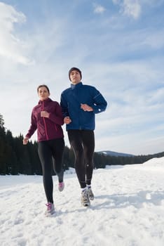 healthy young couple jogging outside on snow in forest. athlete running on  beautiful sunny winter day