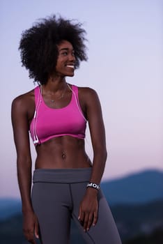portrait of a young beautiful african american woman with headphones jogging in nature beautiful summer night