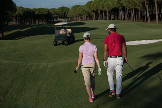 young couple walking to next hole on golf course. man carrying golf bag