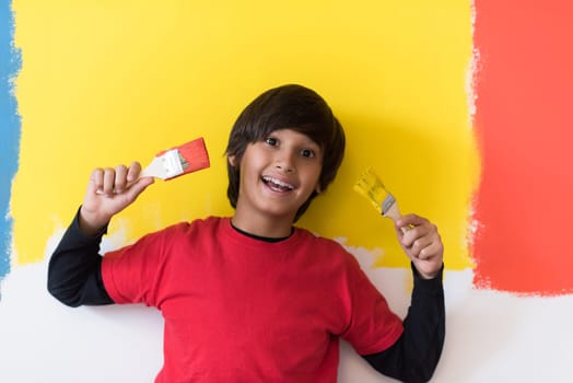 Portrait of a young boy painter with a brushes in his hands in front of colored background