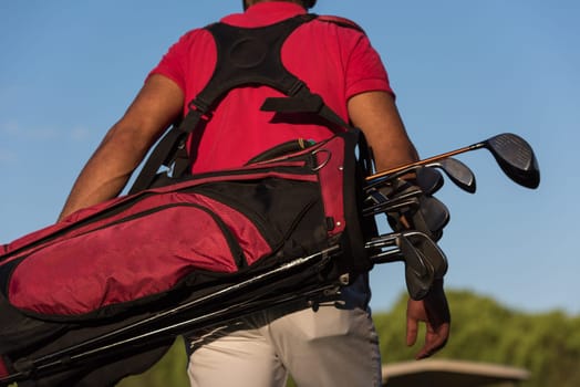 close up of golfers back while carrying  golf bag  and walking at course to next hole