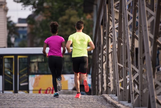 healthy young multiethnic couple jogging across the bridge in the city at early morning with sunrise in background
