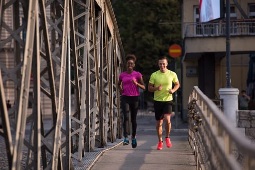 healthy young multiethnic couple jogging across the bridge in the city at early morning with sunrise in background