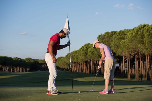 male golf instructor teaching female golf player, personal trainer giving lesson on golf course