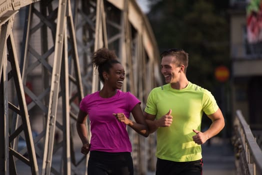 healthy young multiethnic couple jogging across the bridge in the city at early morning with sunrise in background
