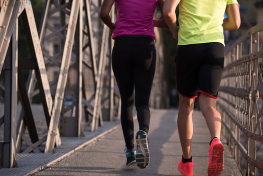 healthy young multiethnic couple jogging across the bridge in the city at early morning with sunrise in background