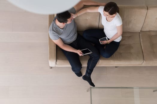 Young couple relaxing at luxurious home with tablet computers reading in the living room on the sofa couch.