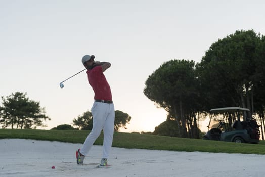 golf player shot ball from sand bunker at course with beautiful sunset with sun flare