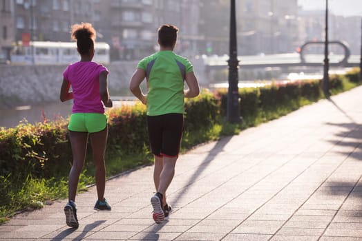 healthy young multiethnic couple jogging in the city at early morning with sunrise in background