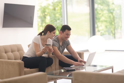 happy young couple buying online using laptop a computer and a credit card in their luxury home villa