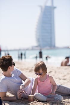 cool young mom and her little girl playing with a bucket full of sand wearing sunglasses and relaxing on the beach on a sunny day