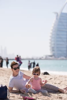 cool young mom and her little girl playing with a bucket full of sand wearing sunglasses and relaxing on the beach on a sunny day