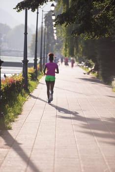 Beautiful young sporty african american woman running at early morning jogging with city sunrise scene in background