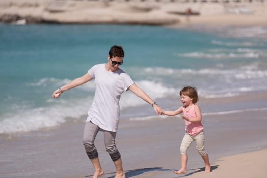 beautiful young mother and cute little girl are enjoying while running on exotic beach along the ocean Travel and Vacations.