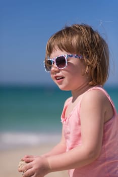 happy little girl at the seaside in the summer.Adorable little girl at beach during summer vacation. Happy baby with sunglasses by the sea or ocean