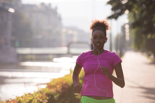 Beautiful young sporty african american woman running at early morning jogging with city sunrise scene in background