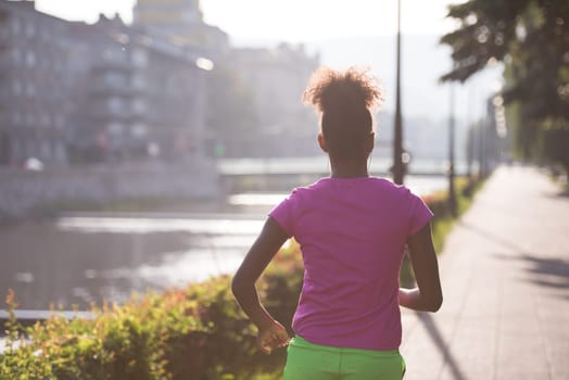 Beautiful young sporty african american woman running at early morning jogging with city sunrise scene in background