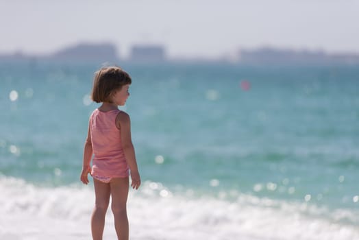 happy little girl at the seaside in the summer.Adorable little girl at beach during summer vacation. Happy baby by the sea or ocean