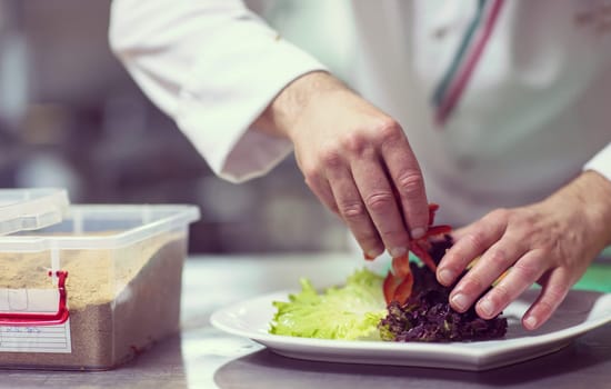 chef serving vegetable salad on plate in restaurant kitchen