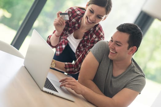 happy young couple buying online using laptop a computer and a credit card in their luxury home villa