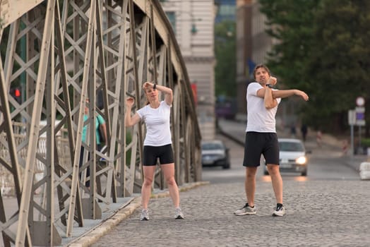 jogging couple warming up and stretching before morning running training workout  in the city with sunrise in background