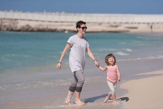 beautiful young mother and cute little girl are enjoying while running on exotic beach along the ocean Travel and Vacations.