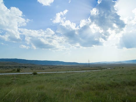 Evening summer landscape with green grass, road and clouds