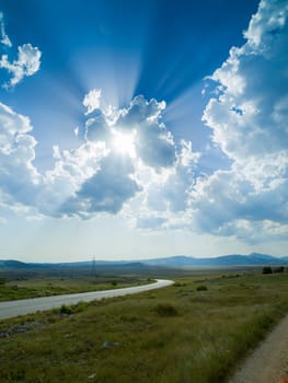 Evening summer landscape with green grass, road and clouds