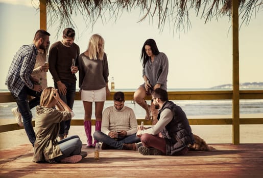 Happy Group Of Friends Hanging Out At Beach House having fun and drinking beer on autumn day colored filter