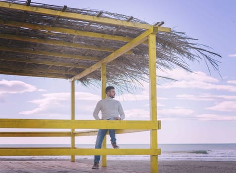 Young man on the beach. The guy enjoying the warm autumn day. Portrait of man near the water colored filter