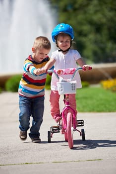 Happy childrens outdoor,  brother and sister in park have fun. Boy and girl in park learning to ride a bike.
