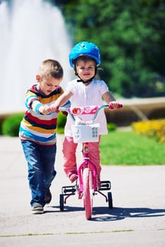 Happy childrens outdoor,  brother and sister in park have fun. Boy and girl in park learning to ride a bike.