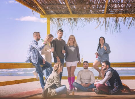 Happy Group Of Friends Hanging Out At Beach House having fun and drinking beer on autumn day colored filter