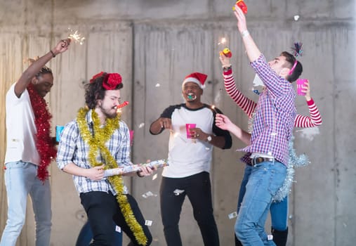 multiethnic group of young happy casual business people dancing and having confetti party while celebrating new year eve in front of concrete wall at new startup office