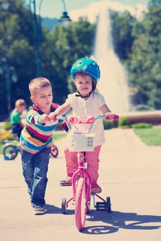 Happy childrens outdoor,  brother and sister in park have fun. Boy and girl in park learning to ride a bike.