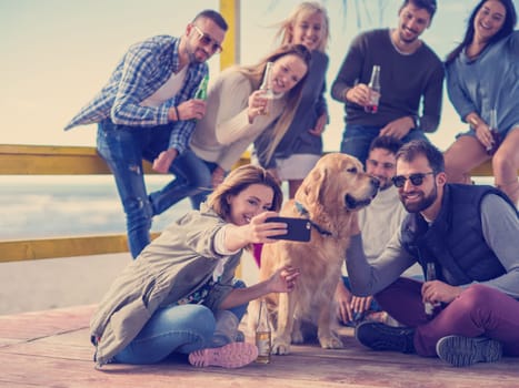 Happy Group Of Friends Hanging Out At Beach House having fun and drinking beer on autumn day