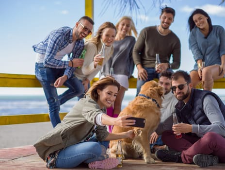 Happy Group Of Friends Hanging Out At Beach House having fun and drinking beer on autumn day