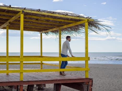 Young man on the beach. The guy enjoying the warm autumn day. Portrait of man near the water