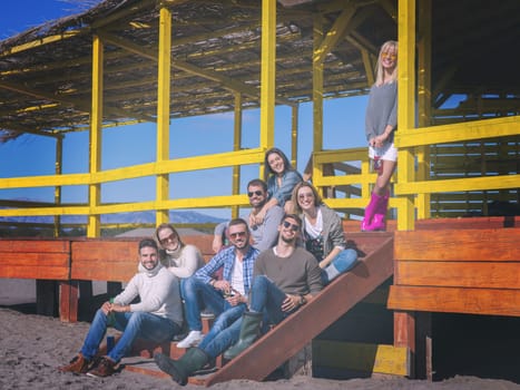 Happy Group Of Friends Hanging Out At Beach House having fun and drinking beer on autumn day colored filter