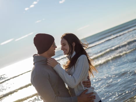 Young couple having fun walking and hugging on beach during autumn sunny day