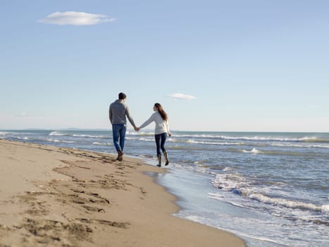 Young couple having fun walking and hugging on beach during autumn sunny day