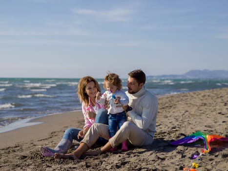 Family with little daughter resting and having fun making soap bubble at beach during autumn day