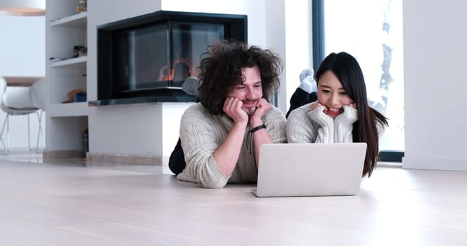 Young beautiful multiethnic couple using a laptop and doing shopping online at home on the floor