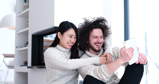 Young beautiful multiethnic couple using a tablet and doing shopping online at home on the floor