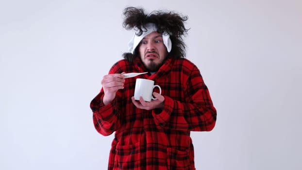 young Man with flu and fever wrapped holding cup of healing tea isolated over white