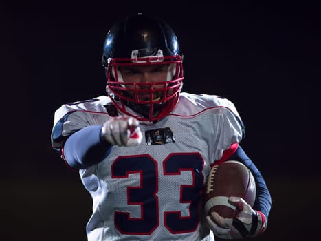 portrait of confident American football player holding ball while standing on field at night