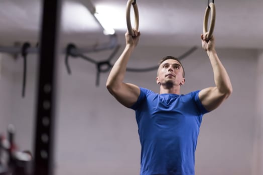Fitness handsome man doing dipping exercise using rings in the gym